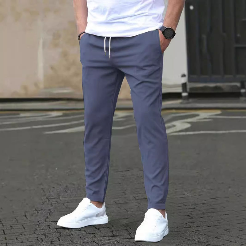 Mann in blauer Jogginghose und weißen Sneakers auf Asphalt, lässiger Stil, moderne Herrenmode, Freizeitkleidung, urbane Umgebung.