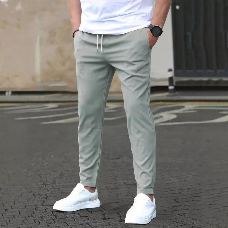 Mann in grauer Jogginghose und weißen Sneakers auf Asphalt, lässiger Stil, moderne Herrenmode, Freizeitlook, urbaner Hintergrund.