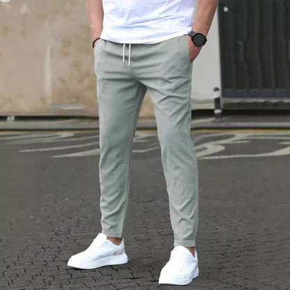 Mann in grauer Jogginghose und weißen Sneakers auf Asphalt, lässiger Stil, moderne Herrenmode, Freizeitlook, urbaner Hintergrund.