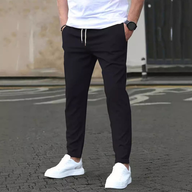 Mann in schwarzer Jogginghose und weißen Sneakers auf Straße. Lässige Herrenmode, sportlicher Look, bequeme Freizeitkleidung.