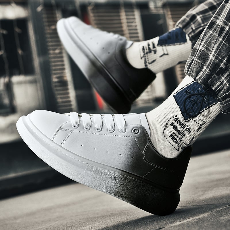 Weiße und schwarze Sneaker auf grauem Hintergrund, getragen mit karierten Hosen und bedruckten Socken. Moderne Straßenschuhe, urbaner Stil.