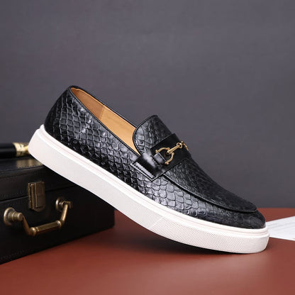 Schwarzer Herren-Loafer mit Schlangenhaut-Textur und goldener Schnalle, auf braunem Koffer. Elegante Herrenschuhe, modisch und stilvoll.