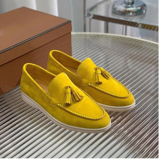 Gelbe Wildleder-Loafer mit Quasten auf einem silbernen Tisch neben einer braunen Box. Modische Herrenschuhe, stilvoll und elegant.