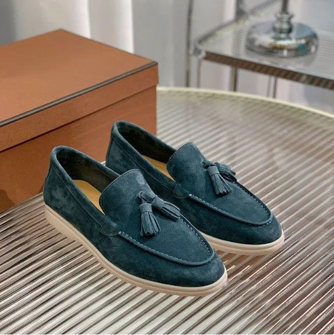Dunkelblaue Wildleder-Slipper mit Quasten auf einem Tisch, neben einer braunen Schuhschachtel. Elegante Herrenschuhe, modern und stilvoll.