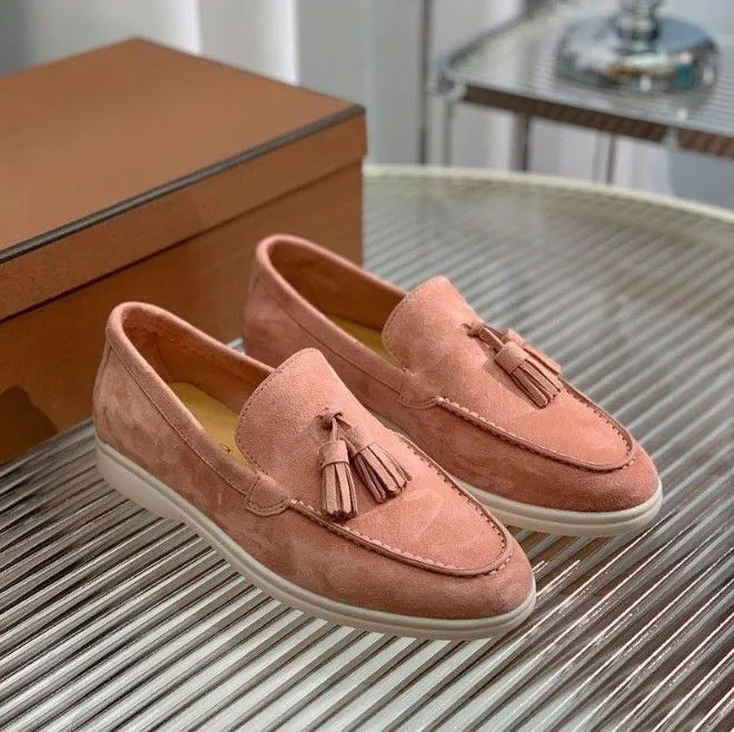 Rosa Wildleder-Loafer mit Quasten auf einem Tisch, neben einer braunen Schuhschachtel. Elegante, bequeme Damenschuhe für Freizeit und Büro.