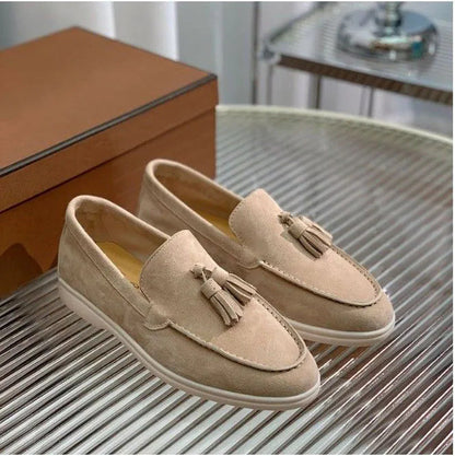 Beige Wildleder-Slipper mit Quasten auf einem gestreiften Tisch, neben einer braunen Box. Elegante Herrenschuhe, ideal für formelle Anlässe.