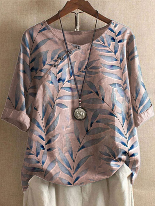 Damenbluse mit blauem Blattmuster, asymmetrischem Kragen und Knopfleiste, kombiniert mit einer langen Halskette. Modetrend 2023, lässiger Stil.