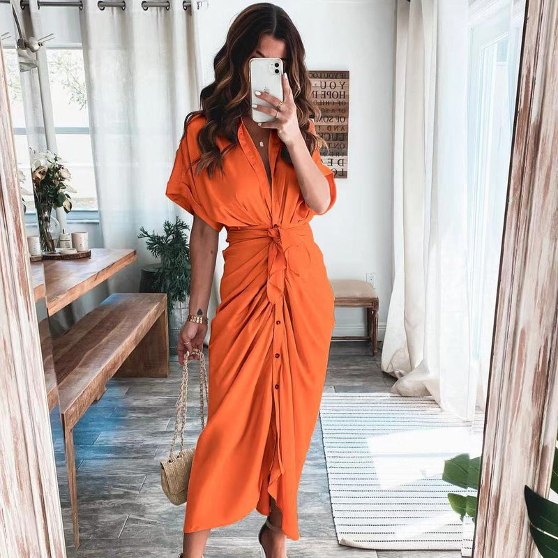 Frau in orangefarbenem Hemdkleid macht Selfie im modernen Wohnzimmer, Holzbank, Pflanzen, Tageslicht, modisches Outfit, Sommermode.
