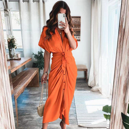 Frau in orangefarbenem Hemdkleid macht Selfie im modernen Wohnzimmer, Holzbank, Pflanzen, Tageslicht, modisches Outfit, Sommermode.