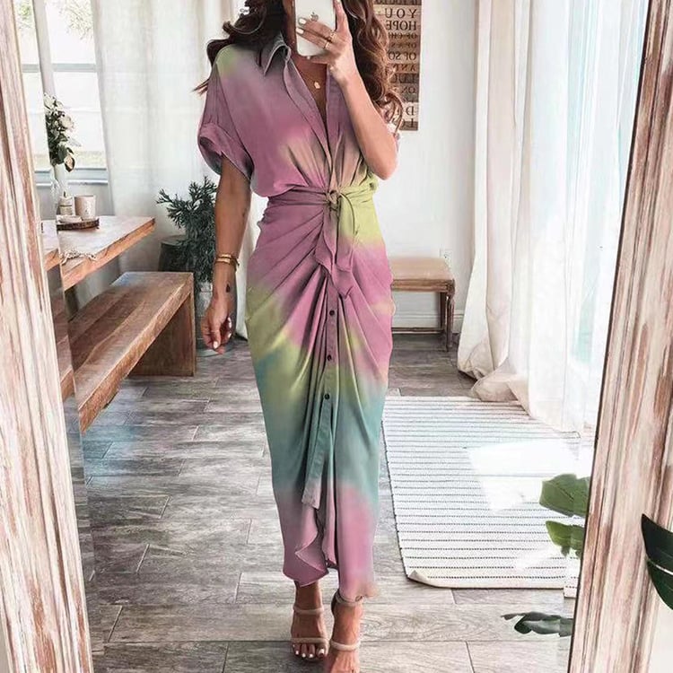 Frau in langem, buntem Kleid mit Knoten-Detail, steht in modernem Wohnzimmer. Sommermode, elegantes Design, trendige Damenbekleidung.