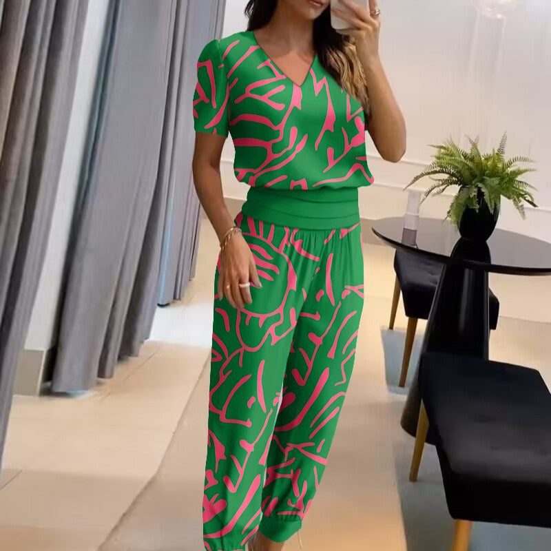 Frau in grünem, gemustertem Jumpsuit mit rosa Akzenten, steht in modernem Wohnzimmer. Stilvolle Mode, trendiges Design, Innenraum.