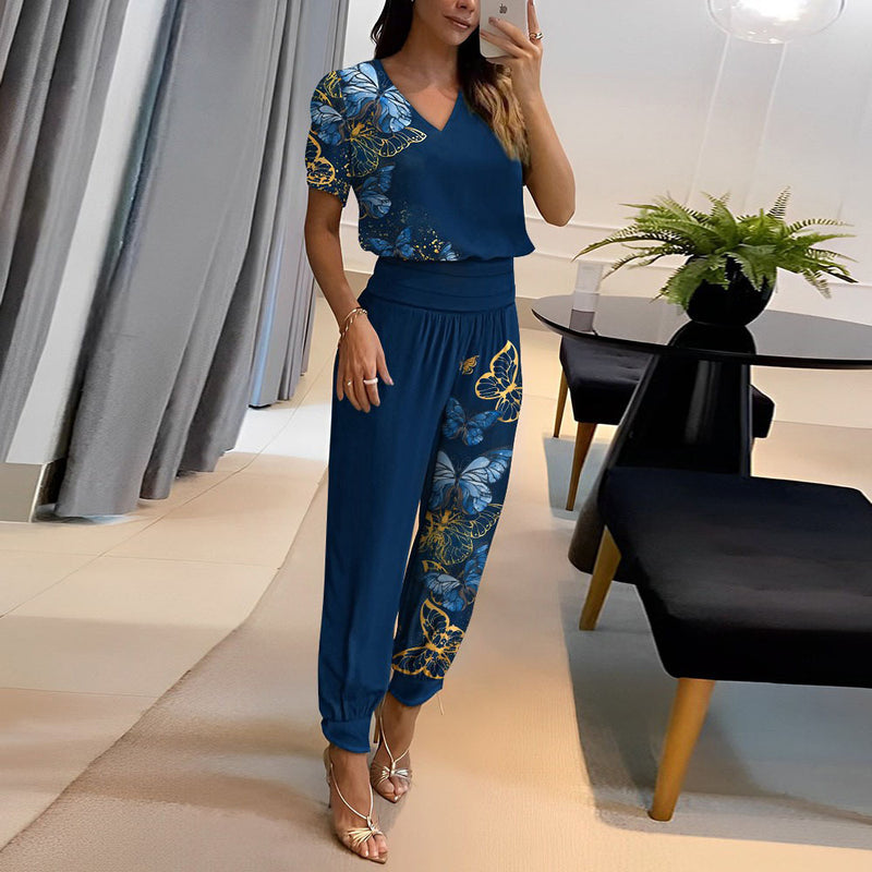 Frau in blauem Jumpsuit mit Schmetterlingsmuster, steht in modernem Wohnzimmer. Elegante Mode, stilvolle Inneneinrichtung, trendige Damenbekleidung.