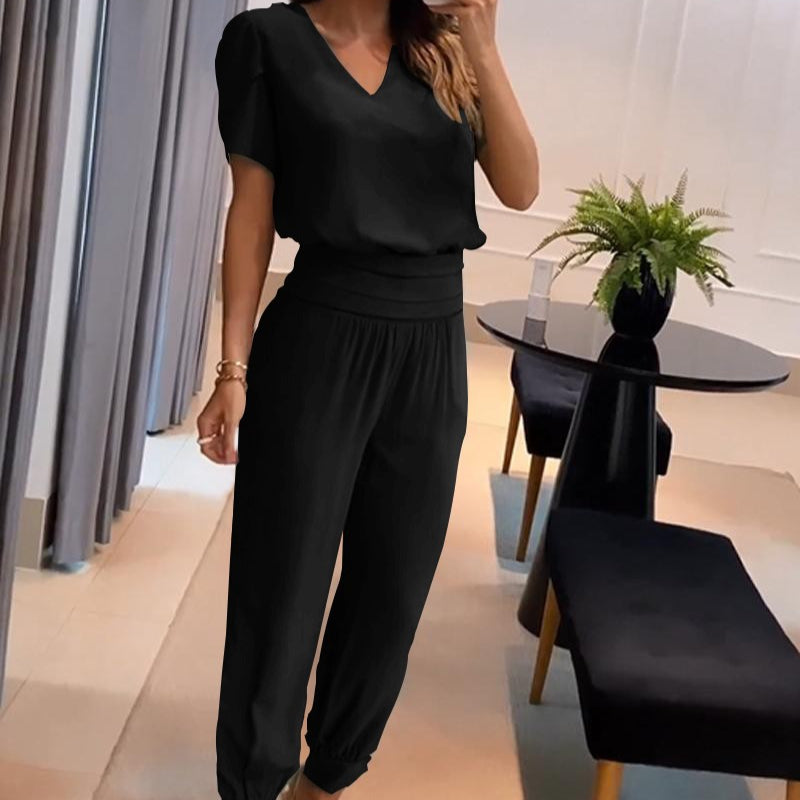 Frau in schwarzem Jumpsuit posiert in modernem Wohnzimmer mit Tisch und Pflanze, elegantes Outfit, Mode, Innenarchitektur, stilvolle Kleidung.