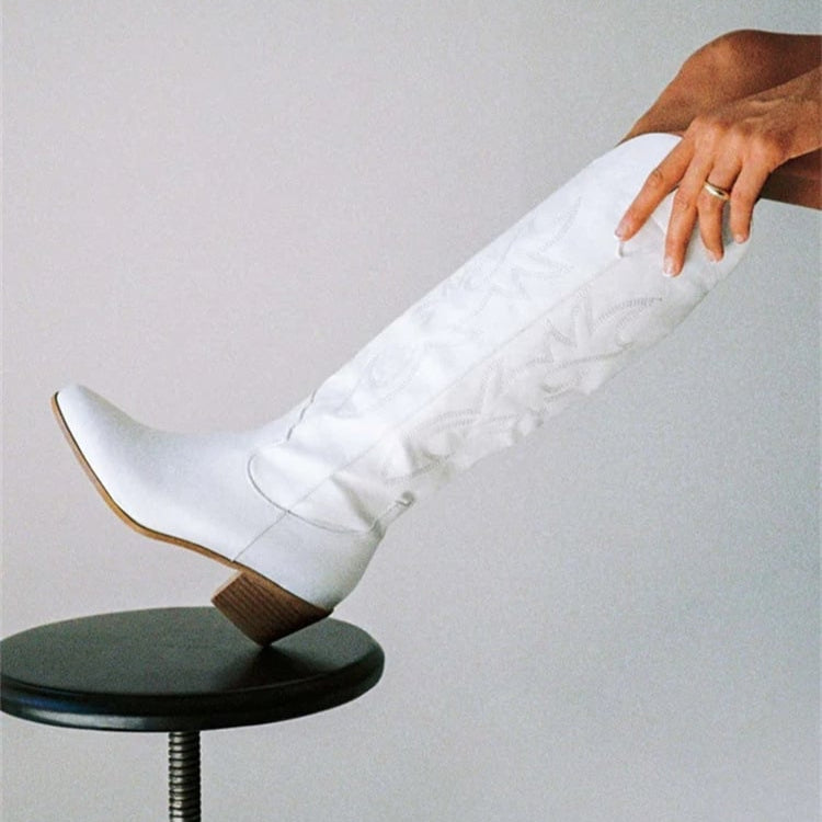 Weiße kniehohe Stiefel mit Absatz auf einem Hocker, Hand berührt den Schaft. Modetrend, Damenstiefel, elegantes Design, stilvolle Fußbekleidung.