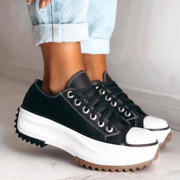 Schwarze Plateau-Sneaker mit weißer Sohle und Zickzack-Profil, getragen von Person in hochgekrempelten Jeans. Trendige Schuhe, modisches Design.