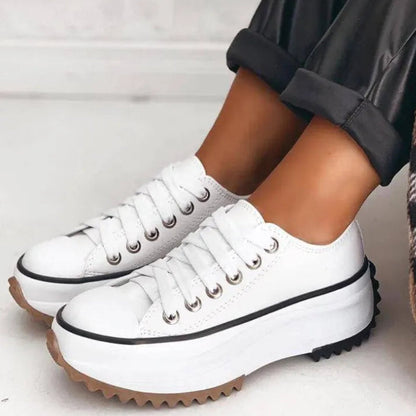 Weiße Plateau-Sneaker mit dicker Sohle und schwarzen Details, getragen von einer Person in schwarzer Hose. Modische Damen-Schuhe, trendiger Look.