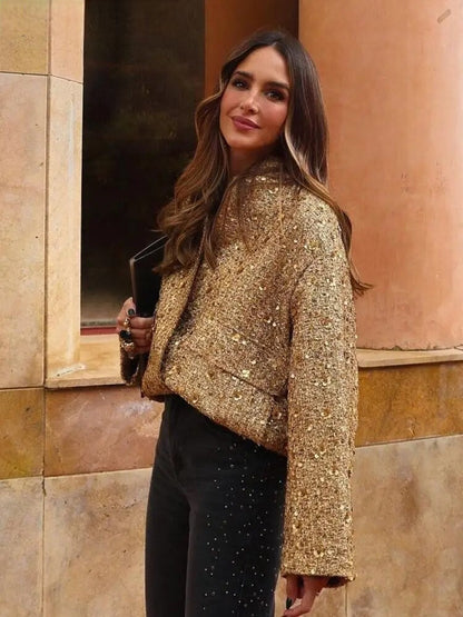 Frau in goldener Glitzerjacke und schwarzer Hose, hält eine schwarze Clutch. Elegante Mode, Streetstyle, Herbstoutfit, trendige Damenbekleidung.