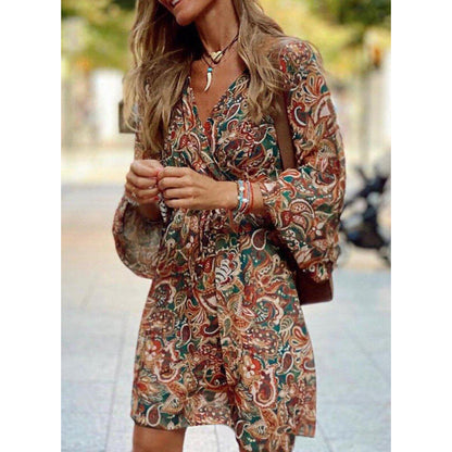 Frau in geblümtem Kleid mit langen Ärmeln, trägt Halskette und Armbänder, steht auf Straße. Modetrend, Herbstkleid, Damenmode, Boho-Stil.