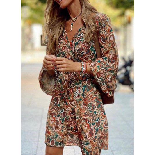 Frau in geblümtem Kleid mit langen Ärmeln, trägt Halskette und Armbänder, steht auf Straße. Modetrend, Herbstkleid, Damenmode, Boho-Stil.