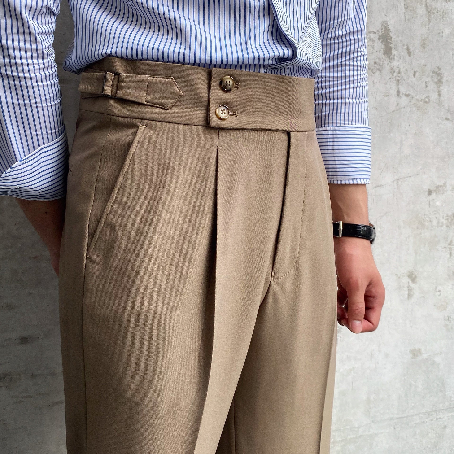 Elegante beige Anzughose mit hoher Taille und Knopfverschluss, getragen von einer Person in gestreiftem Hemd. Modetrend, Herrenmode, Business-Look.