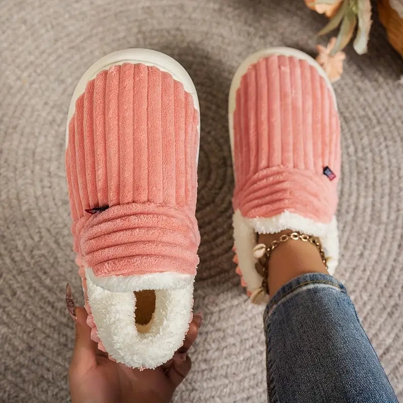 Damen tragen rosa Plüsch-Hausschuhe mit geripptem Design und weißem Futter, auf einem grauen Teppich. Bequeme, warme Hausschuhe für den Winter.