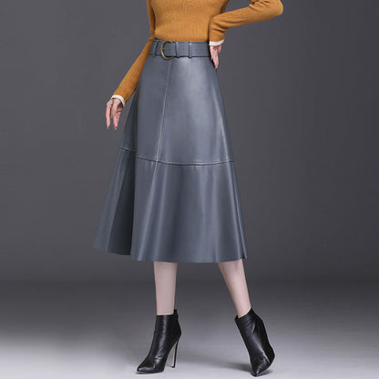 Frau in grauem Lederrock und braunen Pullover, kombiniert mit schwarzen Stiefeletten. Elegante Herbstmode, stilvoller Look, Damenbekleidung.