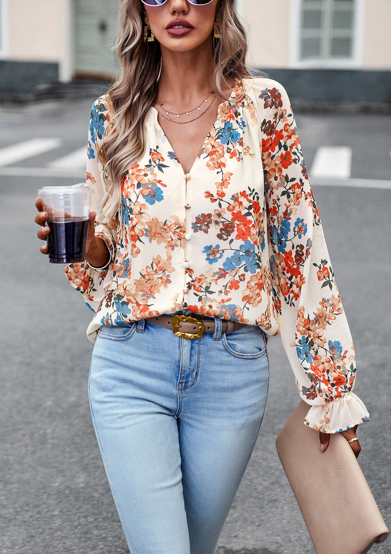 Frau in geblümter Bluse und blauer Jeans, hält Getränk und Tasche, modisch, urbaner Hintergrund, stilvolle Sonnenbrille, lässiger Look.