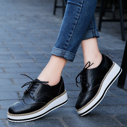 Schwarze Damen-Brogues mit Plateau, geschnürt, aus Leder, kombiniert mit blauen Jeans. Modische Schuhe für Herbst, ideal für urbanen Stil.