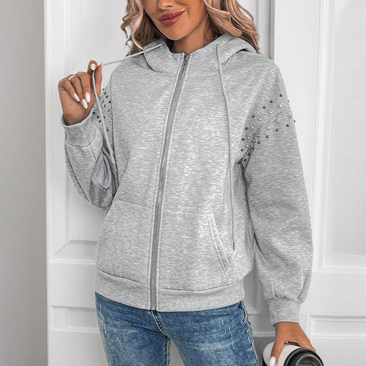 Frau in grauem Kapuzenpullover mit Nieten, lässiger Stil, hält Kaffeebecher, weiße Tür im Hintergrund. Modetrend, Freizeitkleidung, Damenmode.