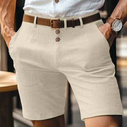 Mann trägt beige Leinen-Shorts mit braunem Ledergürtel und weißem Hemd. Sommermode, Herrenbekleidung, lässiger Stil, Outdoor-Outfit.