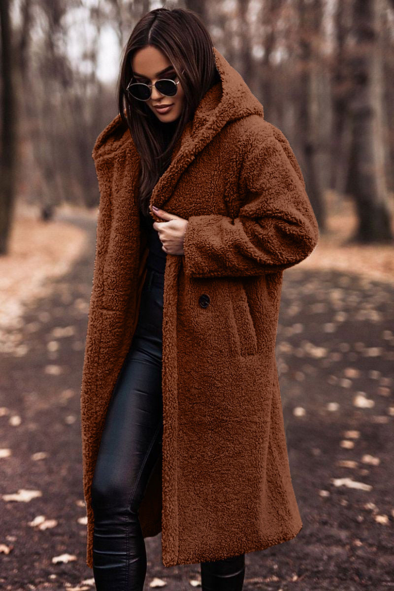 Frau im braunen Teddy-Mantel und Sonnenbrille spaziert im herbstlichen Wald. Modetrend, Herbstmode, stilvolle Damenbekleidung.