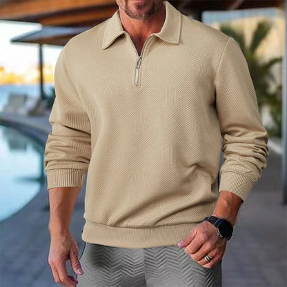 Mann in beigem Pullover mit Reißverschlusskragen, geometrischem Muster, steht vor einem Pool. Stilvolle Herrenmode, Freizeitkleidung, Outdoor.