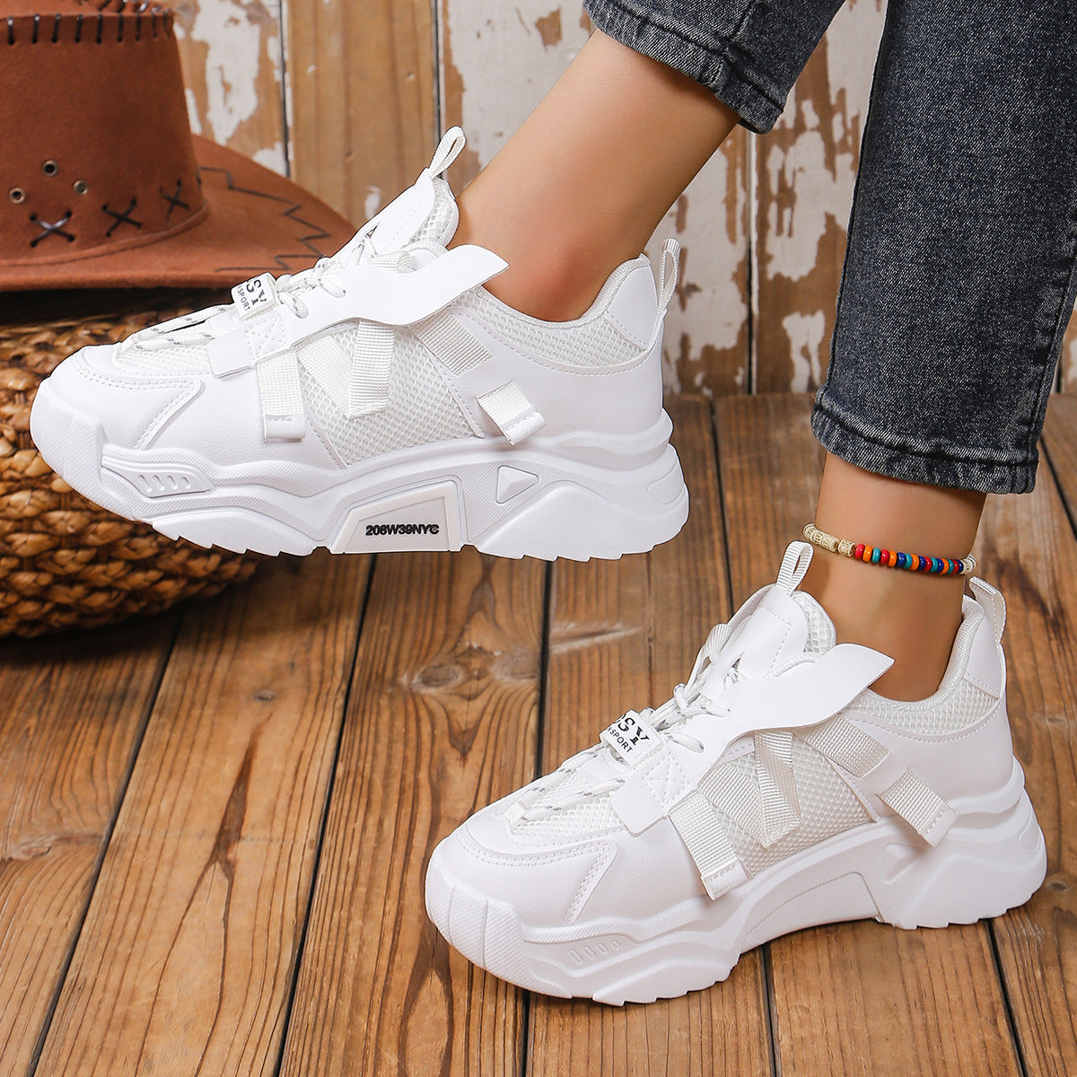 Weiße Damen-Sneaker mit dicker Sohle, getragen auf Holzboden, kombiniert mit Jeans. Modische Sportschuhe, ideal für Freizeit und Streetwear.