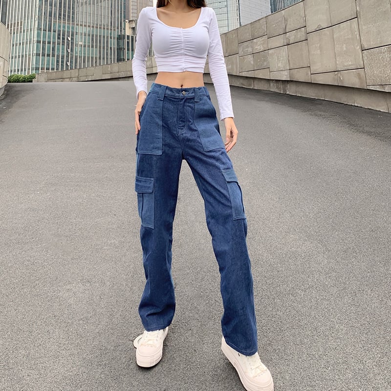 Frau in weißem Crop-Top und blauen Cargo-Jeans auf städtischer Straße. Modetrend, lässiger Stil, urbane Mode, Streetwear, Denim-Look.