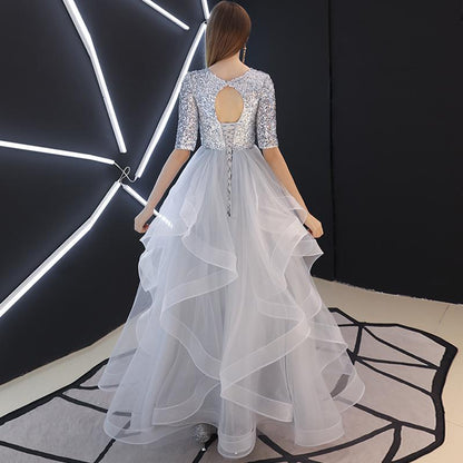 Frau in silbernem Paillettenkleid mit Rückenausschnitt und voluminösem Tüllrock, steht vor moderner, geometrischer LED-Beleuchtung.