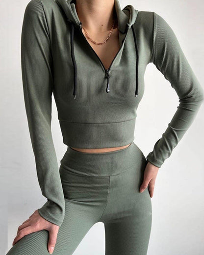 Frau in olivgrünem, geripptem Sport-Set mit Kapuzenpullover und Leggings, modisch und bequem, ideal für Fitness und Freizeit.