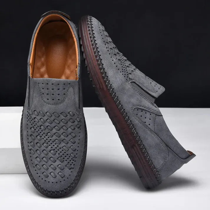 Graue Herren-Loafer aus Wildleder mit perforiertem Design, rutschfester Sohle und braunem Innenfutter auf weißem Hintergrund. Elegante Freizeitschuhe.
