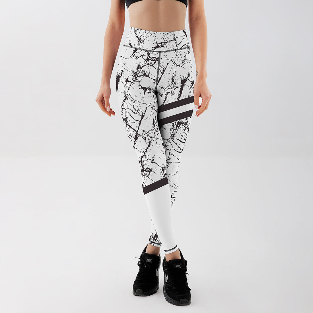 Frau in weißer, marmorierter Sportleggings und schwarzem Top, trägt schwarze Turnschuhe. Fitnessmode, Sportbekleidung, Damenleggings.