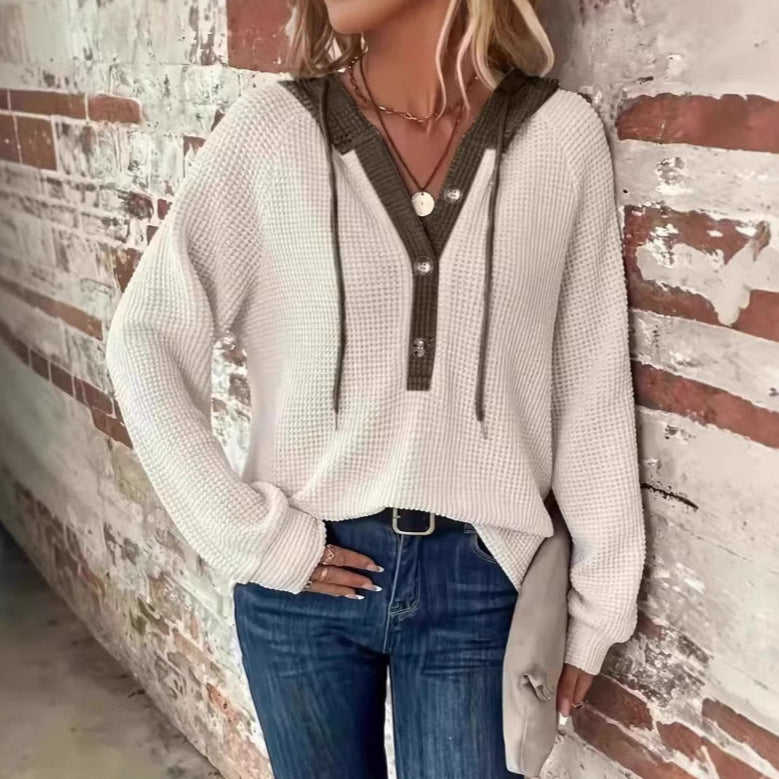 Frau in weißem Strickpullover mit Kapuze und blauen Jeans vor Backsteinwand. Modetrend, lässiger Look, Herbstmode, Damenbekleidung.