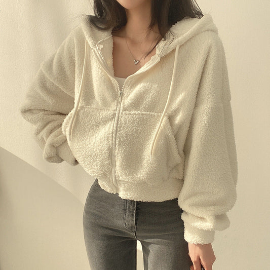 Frau in cremefarbener Teddyfleece-Jacke mit Kapuze und Reißverschluss, kombiniert mit grauer Jeans. Bequeme, modische Winterkleidung.