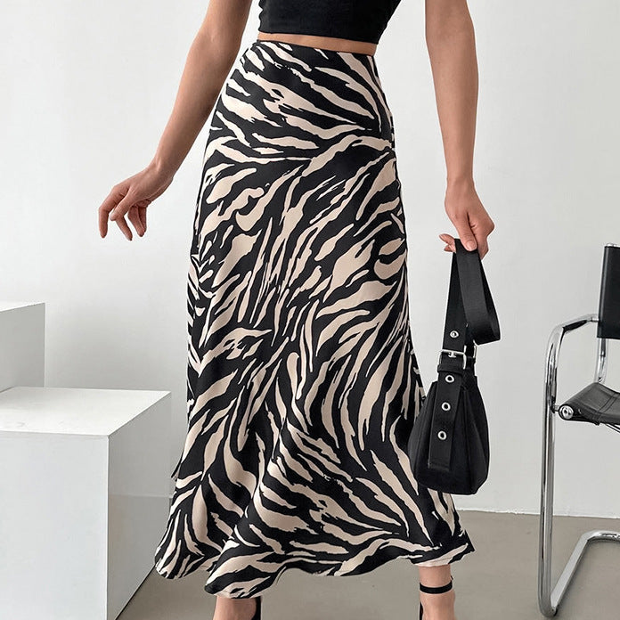 Frau in schwarz-weißem Zebra-Midirock, schwarzem Top und Sandalen, hält schwarze Handtasche. Modetrend, eleganter Look, Sommeroutfit.
