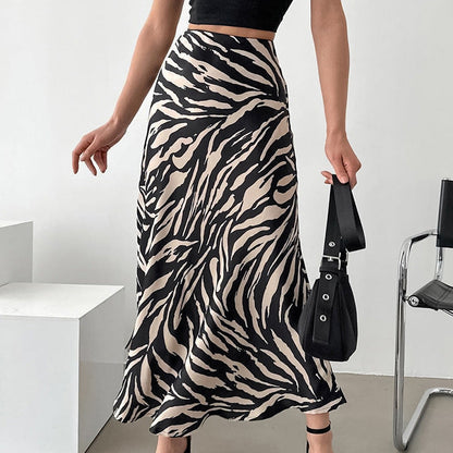 Frau in schwarz-weißem Zebra-Midirock, schwarzem Top und Sandalen, hält schwarze Handtasche. Modetrend, eleganter Look, Sommeroutfit.