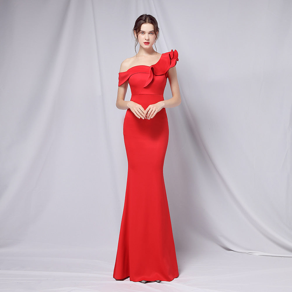 Frau in elegantem, schulterfreiem roten Abendkleid mit Rüschen, posiert vor neutralem Hintergrund. Perfekt für formelle Anlässe und Modeevents.