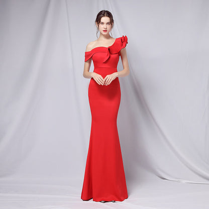 Frau in elegantem, schulterfreiem roten Abendkleid mit Rüschen, posiert vor neutralem Hintergrund. Perfekt für formelle Anlässe und Modeevents.