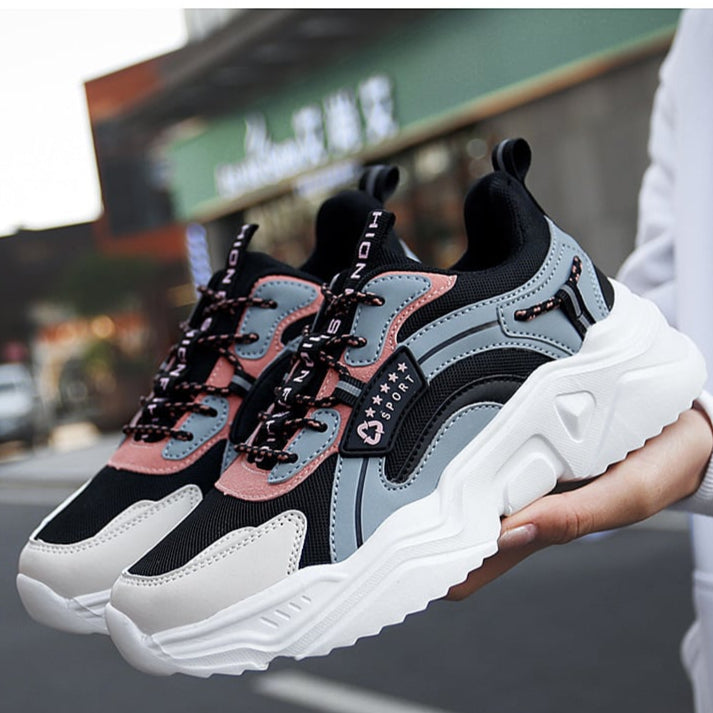 Modische Sneaker in Schwarz, Grau und Rosa mit dicker weißer Sohle, gehalten von einer Hand. Ideal für Streetwear und sportlichen Stil.