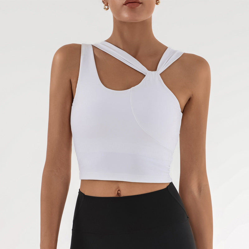 Frau in weißem, asymmetrischem Sport-BH mit überkreuzten Trägern, kombiniert mit schwarzer Leggings. Fitnessmode, Sportbekleidung, Damenoberteil.