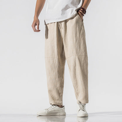 Mann trägt beige Leinenhose, weißes T-Shirt und weiße Sneaker. Modetrend, lässiger Stil, Herrenbekleidung, komfortable Sommermode.