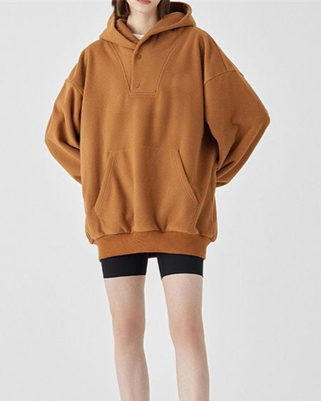 Frau in braunem Oversize-Hoodie und schwarzen Radlerhosen vor weißem Hintergrund. Modetrend, lässiger Stil, bequeme Freizeitkleidung.