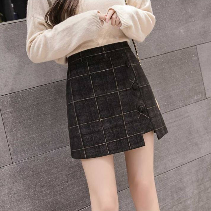 Frau in beigem Pullover und kariertem Rock vor grauer Wand. Modetrend, Herbstmode, Damenbekleidung, eleganter Look, Streetstyle.