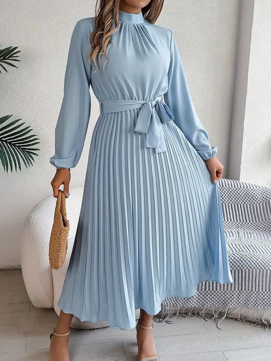 Frau in hellblauem, langärmligem Plisseekleid mit Gürtel, hält eine Strohtasche. Elegantes Outfit, modisch, zeitloses Design.
